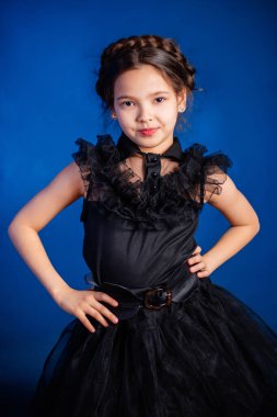 Kafasında örgülü saç stili olan siyah elbiseli küçük bir kızın portresi, koyu bir arka planda, mavi arka planda izole edilmiş.. 