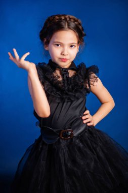 Kafasında örgülü saç stili olan siyah elbiseli küçük bir kızın portresi, koyu bir arka planda, mavi arka planda izole edilmiş.. 