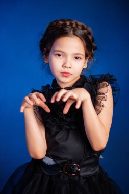 Kafasında örgülü saç stili olan siyah elbiseli küçük bir kızın portresi, koyu bir arka planda, mavi arka planda izole edilmiş.. 