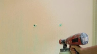 Bir adamın eline yakın plan bir elektrikli sprey tabanca tutar ve duvarı bejle boyar, ses ve yüksek sesli elektrikli bir aletin gürültüsüyle..