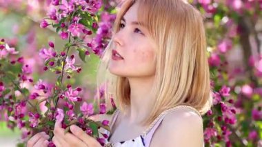 Elinde çiçek açan bir elma ağacının dalını tutan genç bir kadının portresi, pembe çiçeklerin bokeh arka planına karşı.