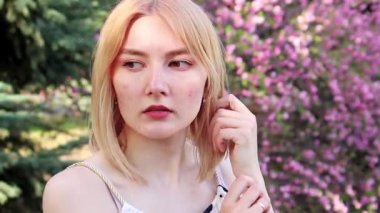 Beyaz elbiseli genç bir kadının portresi, arka planda Sakura 'ya karşı poz veriyor, pembe çiçekli bir bokeh..