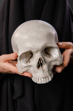 Siyah bornoz giymiş bir kadının elinde bir insan kafatasının yakın çekimi.