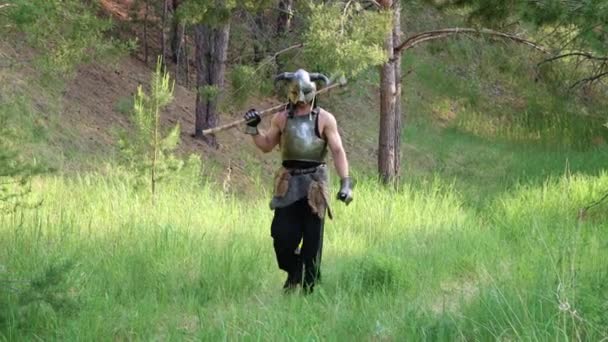 镜头平稳移动 有选择的焦点 一个戴着角形头盔的战士 一个双手拿斧头的钢制胸牌 穿过森林 — 图库视频影像