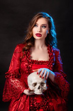 Rokoko döneminde kırmızı elbiseli genç ve çekici bir kadının portresi. Elinde kafatası, mavi arka planda izole bir şekilde poz veriyor..