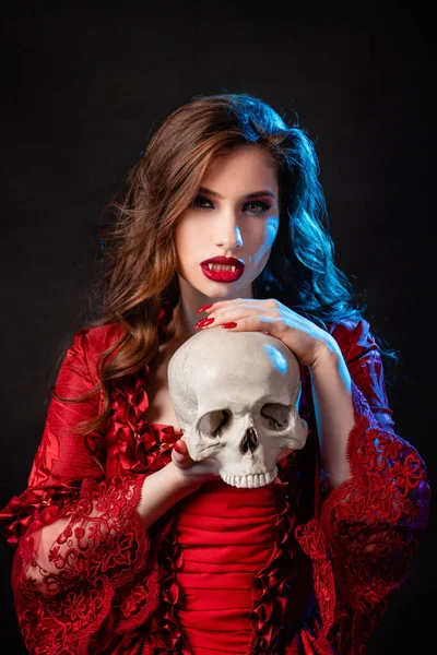在洛可可时代 一个身穿红色裙子的年轻貌美的吸血鬼女子的画像 她双手托着骷髅 背景是深蓝色的背光 — 图库照片
