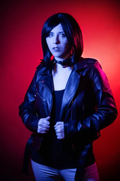 Portrait of young woman with bob haircut in black leather jacket illuminated with blue light posing isolated on dark background with red illumination, cyberpunk concept.