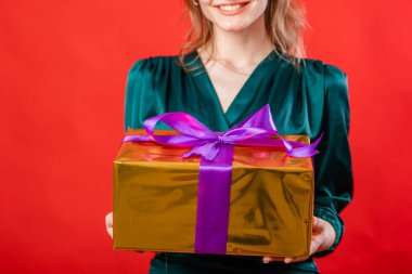 Kırmızı arka planda izole edilmiş genç bir kadının elinde bir yay olan hediye kutusunun yakın çekimi..