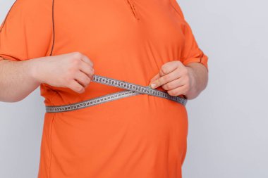 Beyaz arka planda izole edilmiş bir mezura ile göbeğini ölçen bir adama yaklaş.