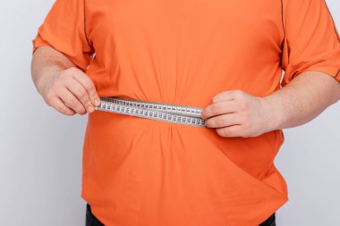 Beyaz arka planda izole edilmiş bir mezura ile göbeğini ölçen bir adama yaklaş.