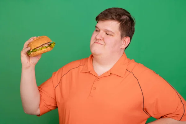 Portrait of a fat guy with a big hamburger in his hands, isolated on a green background. Chroma key, green screen. Fast food and obesity concept.