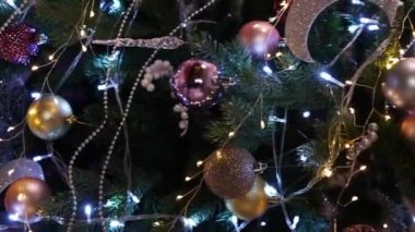 Dikey video, aşağıdan yukarıya düz kamera hareketi, köknar dallarındaki Noel oyuncaklarının yakın çekimi.