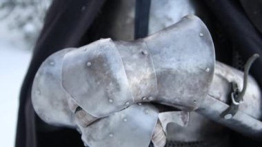 Bir ortaçağ savaşçısının elleri, bir kış ormanının arka planına karşı plaka eldivenli. Kamera hareketi, seçici odak.
