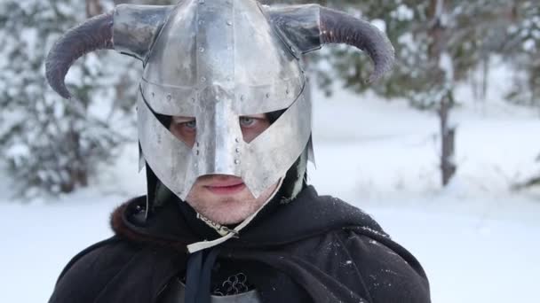 一个戴着角形头盔的中世纪幻想战士的画像 钢制的胸牌 双手拿着一把双手斧子的链子 在冬季森林的背景下摆姿势 照相机运动 — 图库视频影像