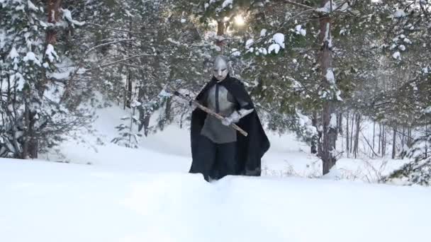 一个戴着角形头盔 手持双手斧头 钢制胸牌和铁链邮件的中世纪幻想战士 在冬季的森林里穿越雪堆 相机移动 选择性聚焦 — 图库视频影像