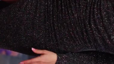 Parlak bir gece elbisesi içinde, bir Noel ağacının arka planında poz veren çekici genç bir kadın. Dikey video, kamera hareketi, seçici odak.