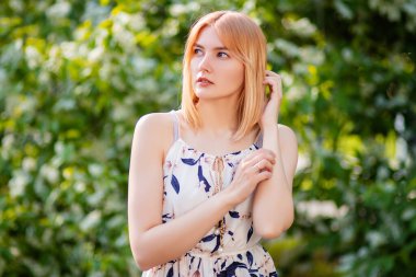 Elbise giymiş çekici bir genç kadının portresi çiçek açan beyaz elma çiçeklerinin arka planında poz veriyor..