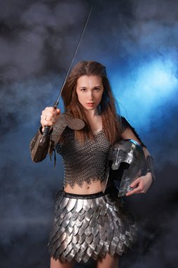 Elinde kılıç ve miğfer olan, koyu bir arka planda mavi bir ışık ile duman içinde duran ortaçağ kadın savaşçısının portresi..