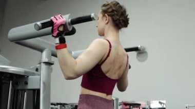 Spor salonundaki bir makinede barfiks çeken genç atletik kadın. Pürüzsüz kamera hareketi, seçici odak.