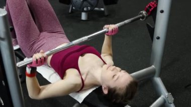 Spor salonundaki bir bankta halter presi yapan genç atletik kadın. Seçici odak yumuşak hareket.