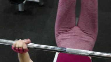 Spor salonundaki bir bankta halter presi yapan genç atletik kadın. Seçici odak yumuşak hareket.