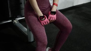 Genç bir atletik kadın spor salonunda egzersiz malzemelerinin arka planında otururken poz veriyor. Kamera hareketi, seçici odak.