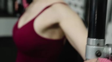 Genç atletik güzel kadın tam teçhizatlı bir spor salonunda göğüs makinesinde egzersiz yapıyor. Seçici odak, kamera hareketi.