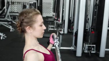 Spor salonundaki bir çekme makinesinde egzersiz yapan atletik genç bir kadın. Seçici odak, kamera hareketi.