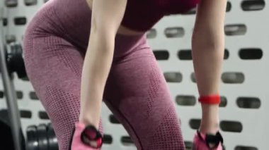 Genç bir atletik kadın spor salonunda halterle ağırlık kaldırma, sırt ve bacak antrenmanı yapıyor. Kamera hareketleri, seçici odaklanma..