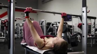 Spor salonundaki bir bankta halter presi yapan genç atletik kadın. Seçici odak yumuşak hareket.