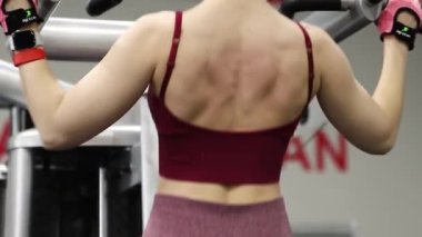 Spor salonundaki bir makinede barfiks çeken genç atletik kadın. Pürüzsüz kamera hareketi, seçici odak.