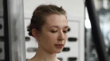 Genç atletik güzel kadın tam teçhizatlı bir spor salonunda göğüs makinesinde egzersiz yapıyor. Seçici odak, kamera hareketi.