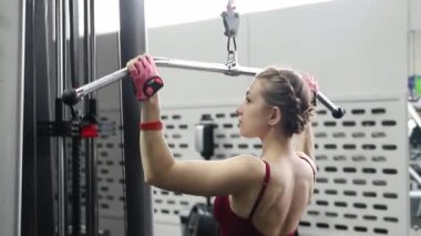 Spor salonundaki bir çekme makinesinde egzersiz yapan atletik genç bir kadın. Seçici odak, kamera hareketi.