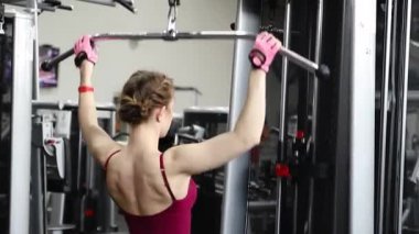 Spor salonundaki bir çekme makinesinde egzersiz yapan atletik genç bir kadın. Seçici odak, kamera hareketi.