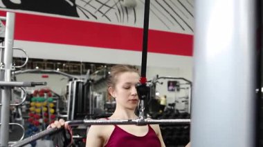 Spor salonundaki bir çekme makinesinde egzersiz yapan atletik genç bir kadın. Seçici odak, kamera hareketi.