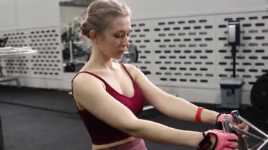 Spor salonundaki bir makinede onu çalıştırmak için egzersiz yapan atletik genç bir kadın. Seçici odak, kamera hareketi.