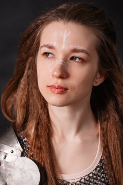 Close up portrait of medieval female warrior in armor with combat makeup on face, isolated on dark background. clipart