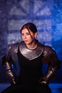 Portrait of a young woman with scars on her face, dressed in black clothes with steel knightly hands and a gorget, posing against an abstract background. Medieval fantasy girl. clipart