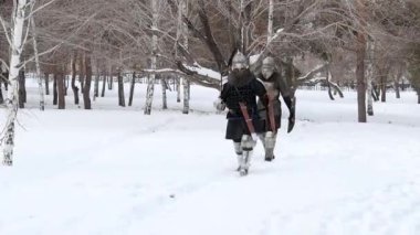 Zırhlı iki ortaçağ savaşçısı bir kış parkında derin karda yürüyorlar. Avrupalı bir şövalye ve Asyalı bir savaşçı seferdeler..