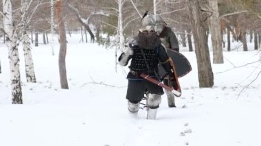 Zırhlı iki ortaçağ savaşçısı bir kış parkında derin karda yürüyorlar. Avrupalı bir şövalye ve Asyalı bir savaşçı seferdeler..