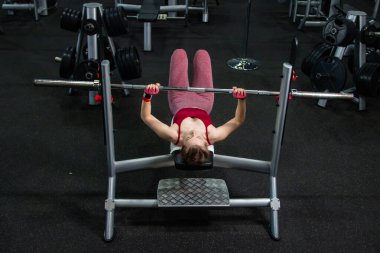 Spor salonundaki bir bankta halterle ağırlık kaldıran genç atletik kadın..