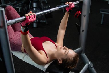 Spor salonundaki bir bankta halterle ağırlık kaldıran genç atletik kadın..