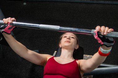 Spor salonundaki bir bankta halterle ağırlık kaldıran genç atletik kadın..