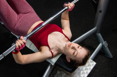 Spor salonundaki bir bankta halterle ağırlık kaldıran genç atletik kadın..