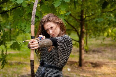 Ortaçağ savaşçısı kadın, zırhlı ve elinde yayıyla yaz ormanı zemininde..