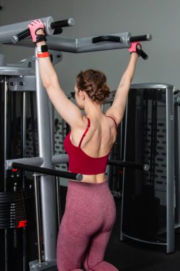 Spor salonundaki bir makinede barfiks çeken genç atletik kadın. Kol ve sırt egzersizi.