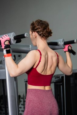 Spor salonundaki bir makinede barfiks çeken genç atletik kadın. Kol ve sırt egzersizi.
