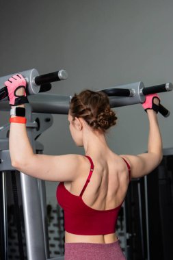 Spor salonundaki bir makinede barfiks çeken genç atletik kadın. Kol ve sırt egzersizi.