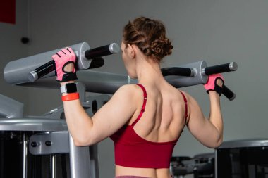 Spor salonundaki bir makinede barfiks çeken genç atletik kadın. Kol ve sırt egzersizi.