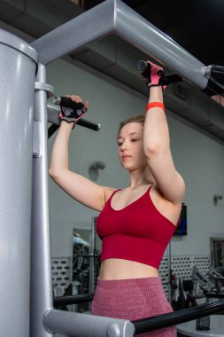 Spor salonundaki bir makinede barfiks çeken genç atletik kadın. Kol ve sırt egzersizi.